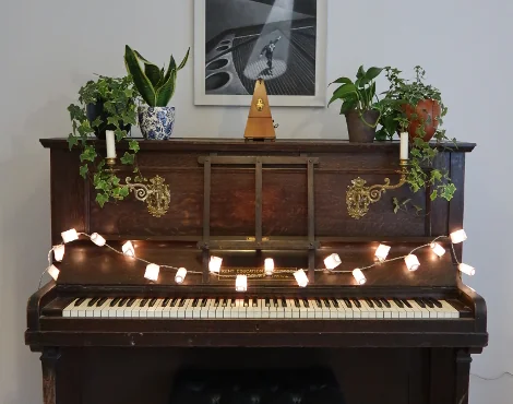 A piano covered in plants and lights. Take Saxophone lessons in London with SaxTeacher UK